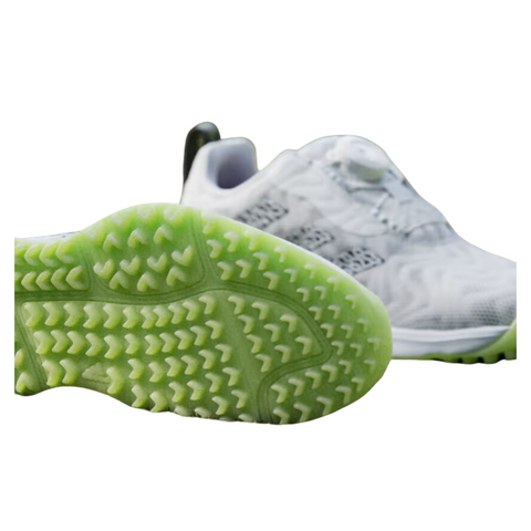 A close-up of two white Adidas 2025 Codechaos BOA Junior Golf Shoes, featuring one in the background and another in front displaying a green textured sole with small raised triangles.