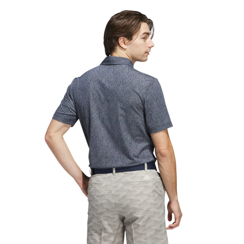 A man with light brown hair wears an Adidas Mens Ultimate365 Bunker Polo Shirt in Collegiate Navy and light gray patterned pants. He stands with his back to the camera, looking left, against a plain white background.