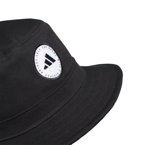 A close-up of the Adidas Solid Bucket Hat in black, ideal for sun protection. It showcases a round white patch with the Adidas logo and text on the front, displayed against a plain white background.