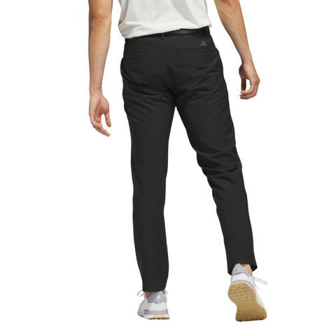 A person is shown from the back, walking forward in a white shirt and Adidas Ultimate365 Mens Golf Pants. They wear white sneakers, set against a plain white background.