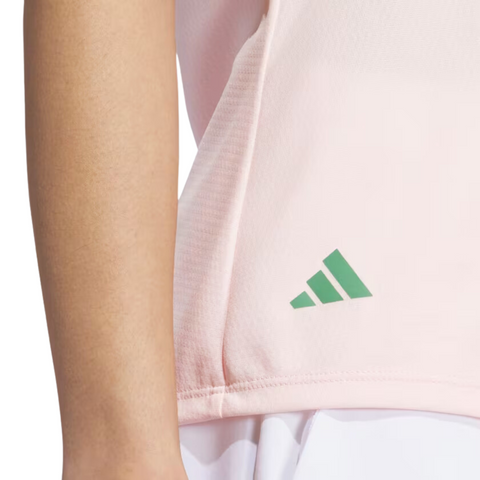 A close-up shows a person in a pale pink Adidas Ultimate365 Womens Printed Polo, featuring a green Adidas logo near the hem. This moisture-wicking golf shirt combines style and comfort for women on the course.