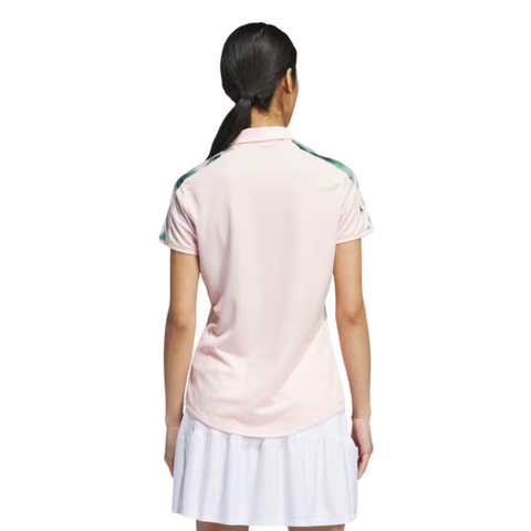 A woman stands with her back to the camera, wearing an Adidas Ultimate365 Womens Printed Polo in light pink and a white pleated skirt, set against a plain white background.