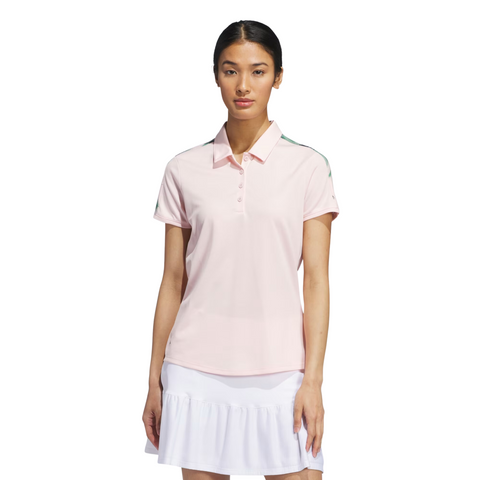 A woman with straight dark hair pulled back stands facing forward in an Adidas Ultimate365 Womens Printed Polo by Adidas and a white ruffled skirt, wearing a neutral expression against a plain white background.