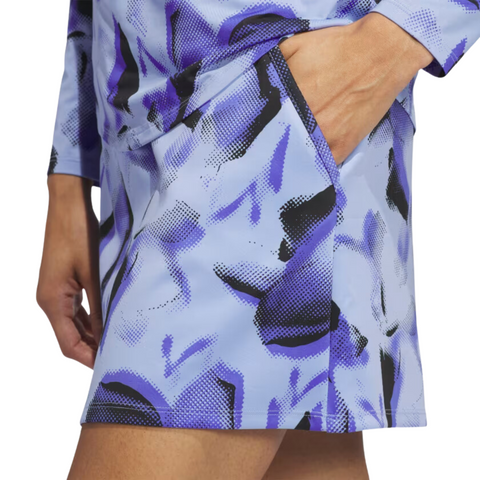 A person wearing the Adidas Ultimate365 Womens Skort by Adidas, shown from waist to mid-thigh, features a light blue and purple abstract pattern with black accents and has their right hand in the pocket.