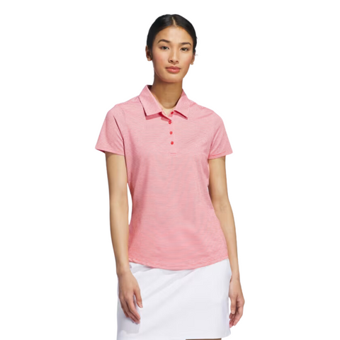 A woman in an Adidas Women's Ottoman Short Sleeve Polo Shirt, pink, and a white skirt stands against a white background, facing forward with a neutral expression.