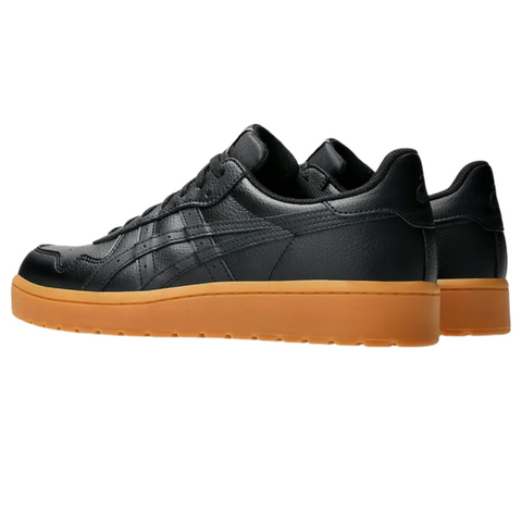The Asics Japan S Mens Golf Shoes by Asics are black leather spikeless shoes with gum rubber soles, pictured from a rear side angle on a white background.