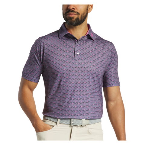 A man in a purple patterned FootJoy Flying Wasp Men’s Lisle Polo, beige pants, and a grey belt stands with one hand on his hip against a white background. This FootJoy golf polo offers moisture-wicking fabric for comfort.