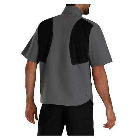 A man stands with his back to the camera wearing a FootJoy HydroLite X Short Sleeve Rain Shirt in gray, featuring black panels on the upper back and shoulders.