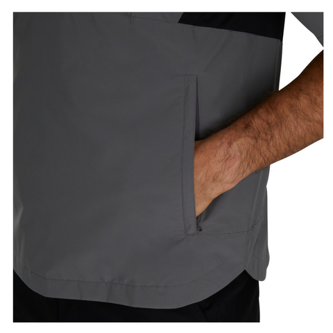 A person wearing a gray FootJoy HydroLite X Short Sleeve Rain Shirt places their right hand in its zippered pocket. Only the lower torso and arm are visible.