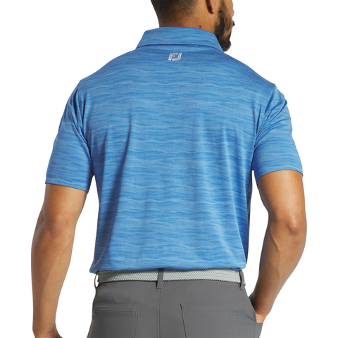 A man is seen from the back wearing a light blue FootJoy Jacquard Wave Mens Polo with short sleeves and gray pants. The polo features a subtle wave pattern and a small FootJoy logo below the collar on the upper back.