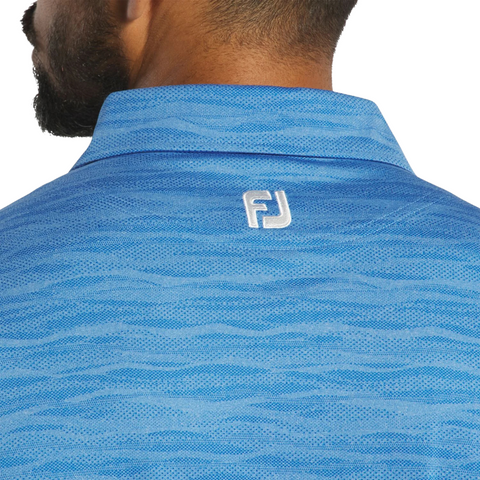 The back view of a person wearing the FootJoy Jacquard Wave Mens Polo, featuring a blue textured design and the white FootJoy “FJ” logo embroidered below the collar.