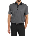 A man wears a FootJoy Men's Checker Print Lisle Polo in black/grey with a black collar, paired with black pants and a black belt. The polo is crafted from lightweight Lisle fabric. His face is not visible.