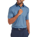 A man wearing a FootJoy Men's Checker Print Lisle Polo in Dark Denim/White and dark blue pants, smiling while holding a button near the collar. The polo features moisture-wicking fabric. Plain white background.