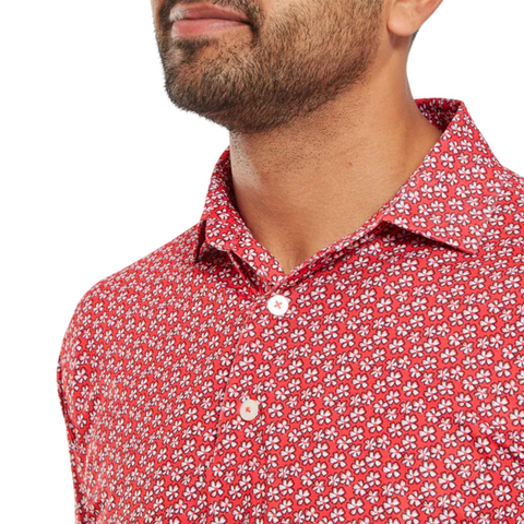 A person wears a FootJoy Men's Floral Sketch Print Lisle Polo in Hibiscus/White, showing the red collar and white-pink floral sketch print. The image highlights the shirt’s collar and upper chest; the face is partially out of frame.
