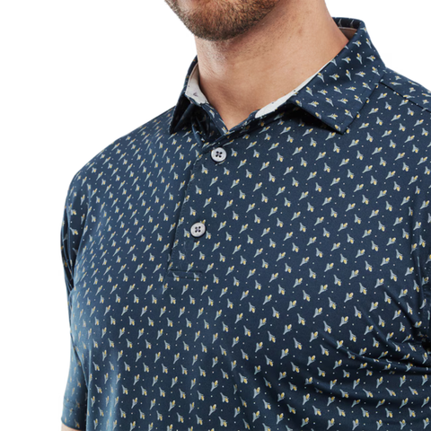A close-up of a man wearing the FootJoy Men's Flower Bud Foulard Lisle Polo in navy, showcasing its white and yellow floral print and ProDry performance fabric. The image is cropped at his mouth and mid-torso to highlight the shirt’s subtle design.
