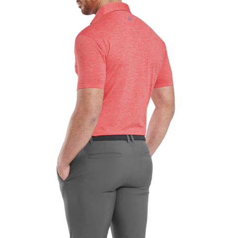 A man stands facing away against a white background, wearing the FootJoy Men's Heather Lisle Polo in Hibiscus tucked into gray pants with a black belt, his left hand in his pocket.