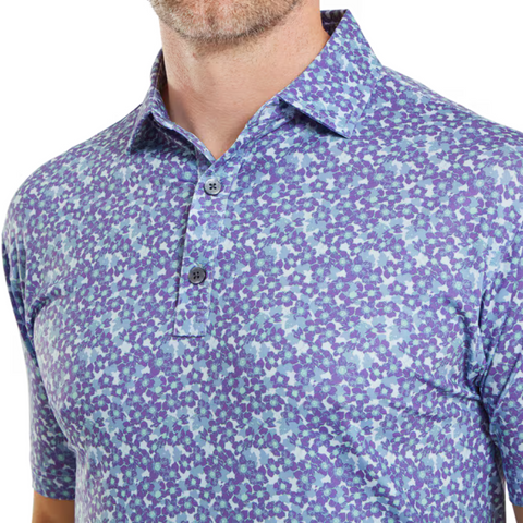 A close-up shows a man in the FootJoy Primrose Print Lisle Mens Polo, a blue and purple golf shirt featuring a collar and two buttons, with only his lower face and upper torso visible.