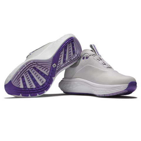 A pair of FootJoy Quantum Womens Golf Shoes in white with purple soles, featuring a spikeless tread—one shoe stands upright while the other lies on its side to show the sole pattern. Brand: FootJoy.