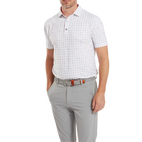 A man wears a FootJoy The 19th Hole Lisle Mens Polo, a white patterned golf shirt by FootJoy, tucked into light gray trousers with a woven belt, standing confidently with one hand in his pocket.