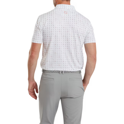 A man stands facing away, wearing a FootJoy The 19th Hole Lisle Mens Polo—a white patterned short-sleeve golf shirt—tucked into light gray pants with a black and white belt. His arms hang relaxed at his sides.