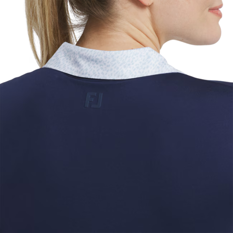 A close-up of a woman's neck and shoulder, wearing the FootJoy Women’s Cap Sleeve Print Shirt in Navy/Skyway, featuring a patterned collar, cap sleeves, and the FJ logo on the back.