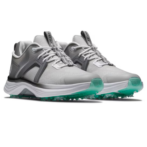 The FootJoy Women's Hyperflex Golf Shoes in Grey/Teal feature white midsoles, translucent teal outsoles, and dark gray accents—lightweight shoes displayed at an angle to showcase comfort and style on the course.