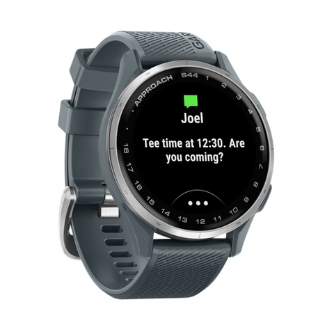 A grey Garmin Approach S44 GPS Watch by Garmin shows Joel’s message—“Tee time at 12:30. Are you coming?”—on its round display, seamlessly combining smart notifications with advanced golf technology.