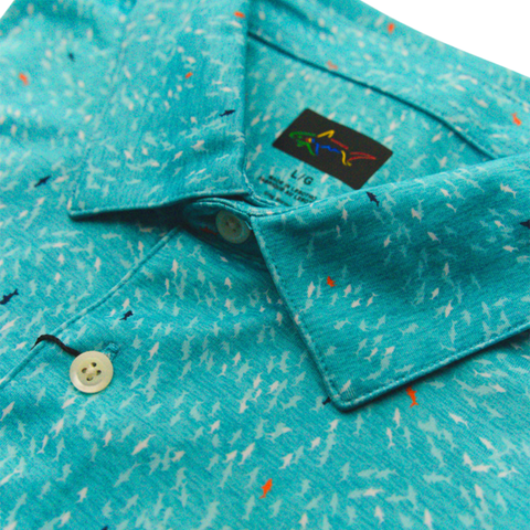 A close-up of the Greg Norman Men’s ML75 Shark Frenzy Print Polo in Aquamarine, a lightweight, moisture-wicking golf shirt with a white, blue, and orange shark pattern, white buttons, and a multicolored shark logo tag.