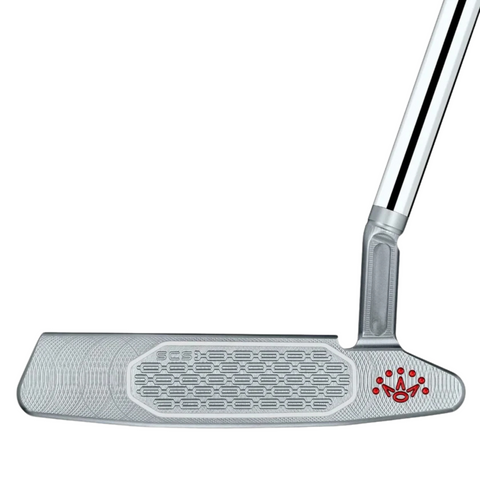 A close-up of the Scotty Cameron 2025 Studio Style Newport 2.5 Plus Putter shows its precision-milled, textured face with detailed pattern, red crown logo near the hosel, and an angled chrome shaft.