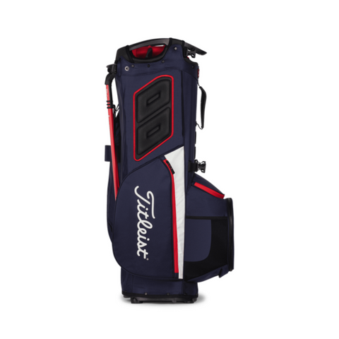 The Titleist Hybrid 14 Golf Bag by Titleist is shown upright on a white background, featuring navy blue color with red and white accents, multiple zippered pockets, a padded shoulder strap, and a 14-way top divider.