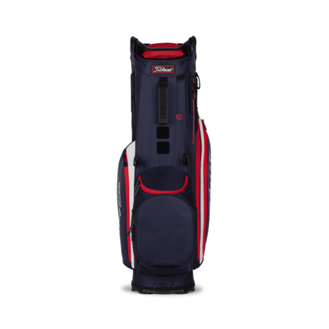A Titleist Hybrid 14 Golf Bag by Titleist, in navy blue with red and white accents, stands upright on a white background. It features a 14-way top divider, several zipper pockets, and a sturdy base.