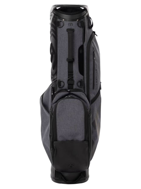 The Travis Mathew Golf BYOB Stand Bag in heather dark grey stands upright, featuring multiple zippered compartments, a padded top for club protection, sturdy handles, and a sleek, modern Travis Mathew design.