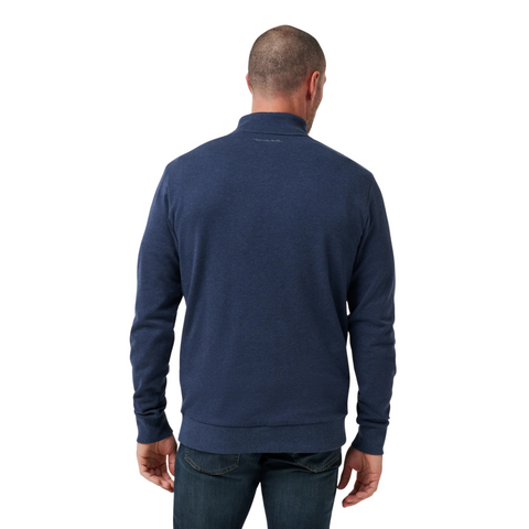 A man with short hair, seen from behind, is wearing a Travis Mathew Cloud 1/4 Zip 2.0 Men’s Pullover in Heather Blue and blue jeans against a plain white background.
