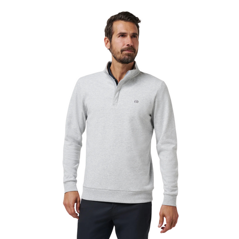 A man stands with a slight smile against a white background, wearing the Travis Mathew Cloud 1/4 Zip 2.0 Men’s Pullover in Heather Light Grey with a small left chest logo and dark pants.