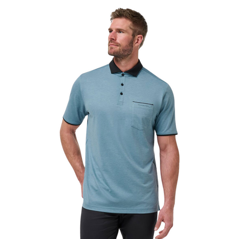 A man with short hair and a beard wears a light blue Travis Mathew Featherweight Pocket Mens Polo featuring a black collar and trim, paired with black pants, looking slightly left against a white background.