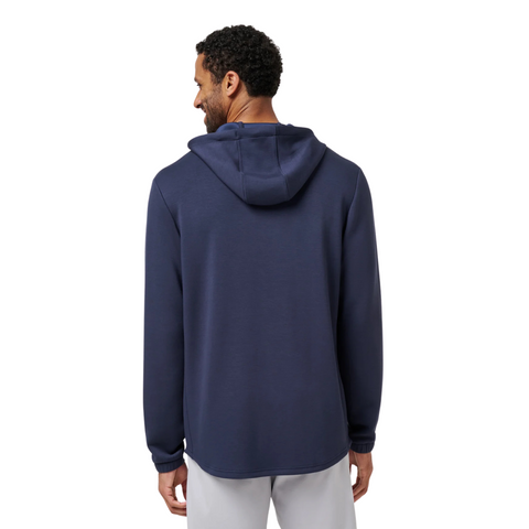 A man stands with his back to the camera, wearing a Travis Mathew Cloud 1/4 Zip 2.0 Men’s Pullover in Heather Blue and light-colored pants against a plain white background.