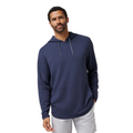 A man wearing a TravisMathew Cloud 1/4 Zip 2.0 Men’s Pullover in Heather Blue and light gray shorts stands against a plain white background.