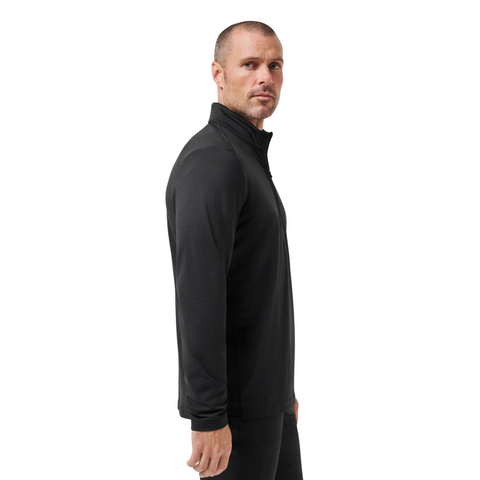 A man with short hair and a trimmed beard stands sideways, wearing the Travis Mathew Heater Pro 1/4 Zip Men’s Pullover in black and black pants, against a plain white background.