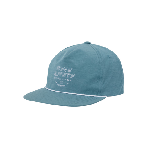 The TravisMathew Hidden Agenda Snapback Cap by Travis Mathew features teal fabric, white stitching, Travis Mathew Established 2007 Designed in CA front embroidery, a curved brim, a snapback closure, and a decorative white line above the brim.