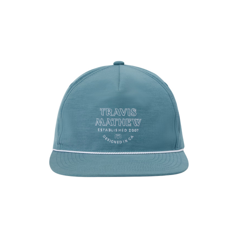 The TravisMathew Hidden Agenda Snapback Cap by Travis Mathew is a blue adjustable golf hat with white trim, featuring TRAVIS MATHEW ESTABLISHED 2007 DESIGNED IN CA embroidered on the front, shown against a white background.