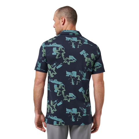 A man with short hair stands with his back to the camera, wearing a Travis Mathew Men’s Favourite Hello Polo in Total Eclipse Blue and light gray pants.