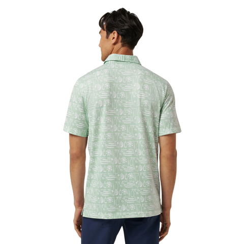 A man with dark hair faces away in the TravisMathew Men’s Featherweight Cabana Polo in Aqua Foam, an ultra-light golf shirt with a white tropical print from Travis Mathew, paired with dark blue pants against a plain white background.