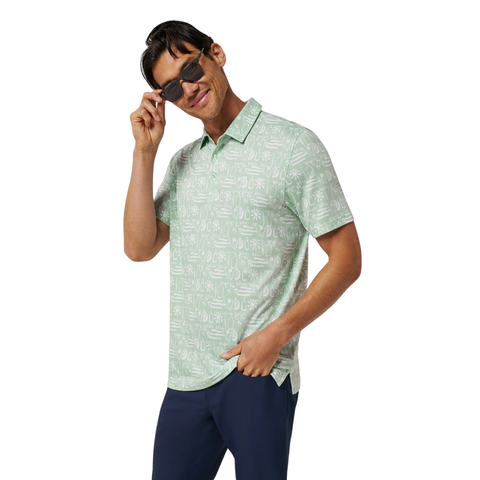 A man in Travis Mathew’s TravisMathew Men’s Featherweight Cabana Polo in Aqua Foam, sunglasses, and dark pants stands against a white background, smiling and holding his sunglasses with one hand.