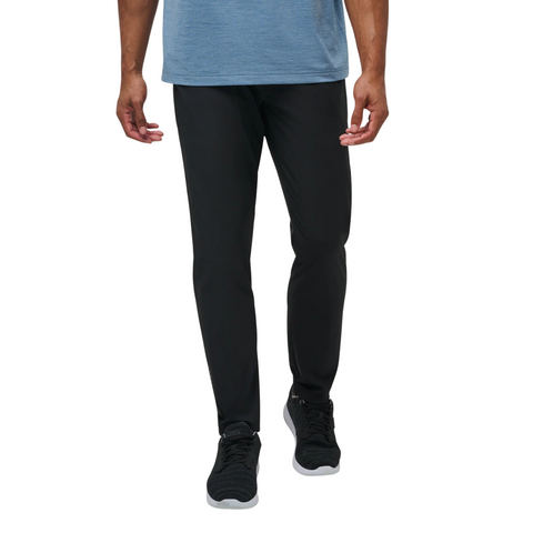 A person in a blue shirt, Travis Mathew Open To Close Men’s Jogger in black, and black sneakers with white soles, shown from shoulders down against a plain white background.