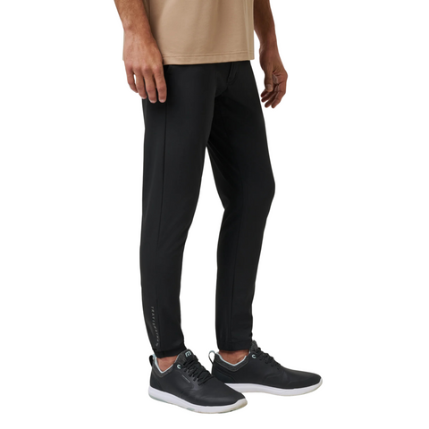 A person wears Travis Mathew Open To Close Men’s Joggers in black with black sneakers on a white background. Only the lower half is visible, highlighting these joggers designed for all-day comfort and modern style.
