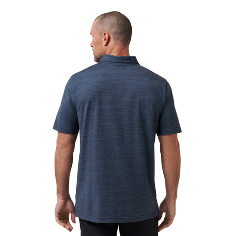 A man with short hair faces away from the camera, wearing a Travis Mathew The Heater Mens Polo and black pants against a plain white background.