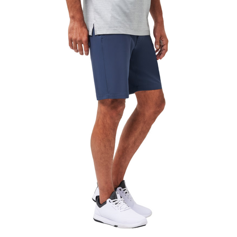 A person in a light gray T-shirt and white sneakers stands against a white background. Only the lower half, showcasing Travis Mathew Wanderlust Mens Shorts, is visible.