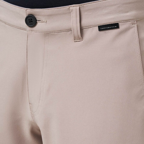 Close-up of Travis Mathew Wanderlust Mens Shorts in beige featuring a black button, belt loop, and a small black waistband label—versatile lightweight shorts ideal for golf or daily wear.