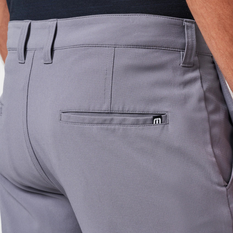 Close-up of the back of a person wearing TravisMathew Wanderlust Mens Shorts with belt loops, a back pocket with a black and white tag, and hands in the front pockets—ideal for golf or casual outings.