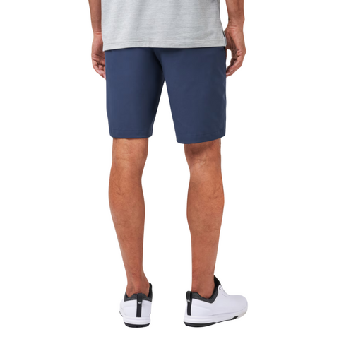A person in a gray shirt, Travis Mathew Wanderlust Mens Shorts in navy blue, and white athletic shoes stands with their back to the camera.
